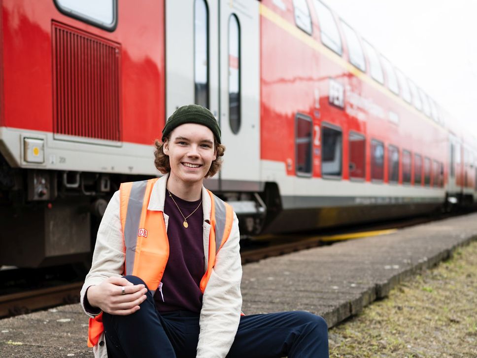 Ein freundlich blickender Auszubildender sitzt vor einem roten Zug.