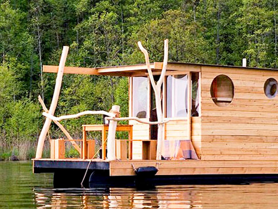 Ein hölzernes Floß mit Terrasse vorne fährt auf dem Wasser.