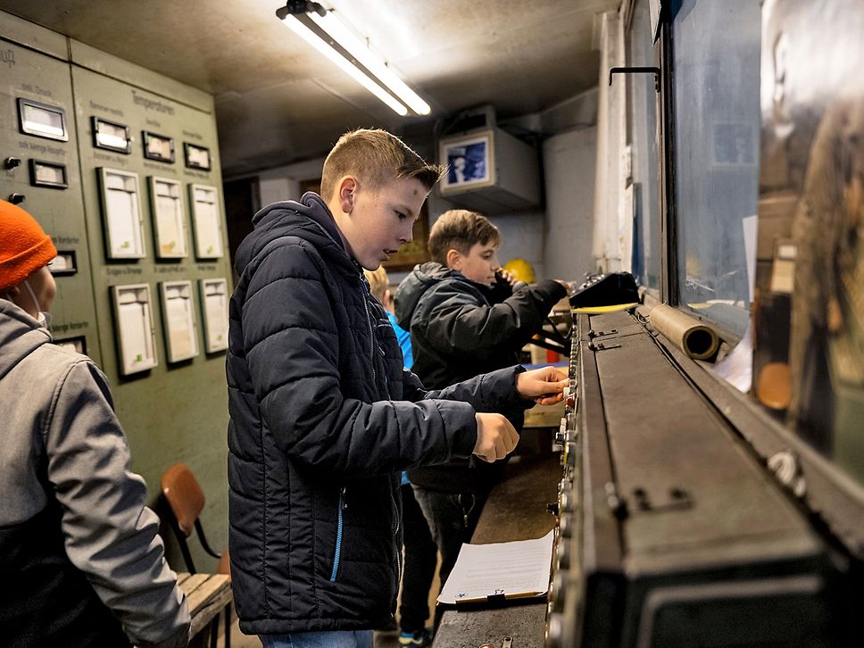 Mehrere Kinder drücken Knöpfe auf einem alten Steuergerät einer Leitstelle.