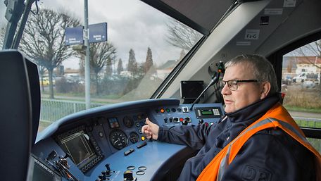 Zugbereitsteller Frank Weiß im Führerstand eines Zuges. Er trägt Brille, eine blaue Jacke und eine Warnweste.