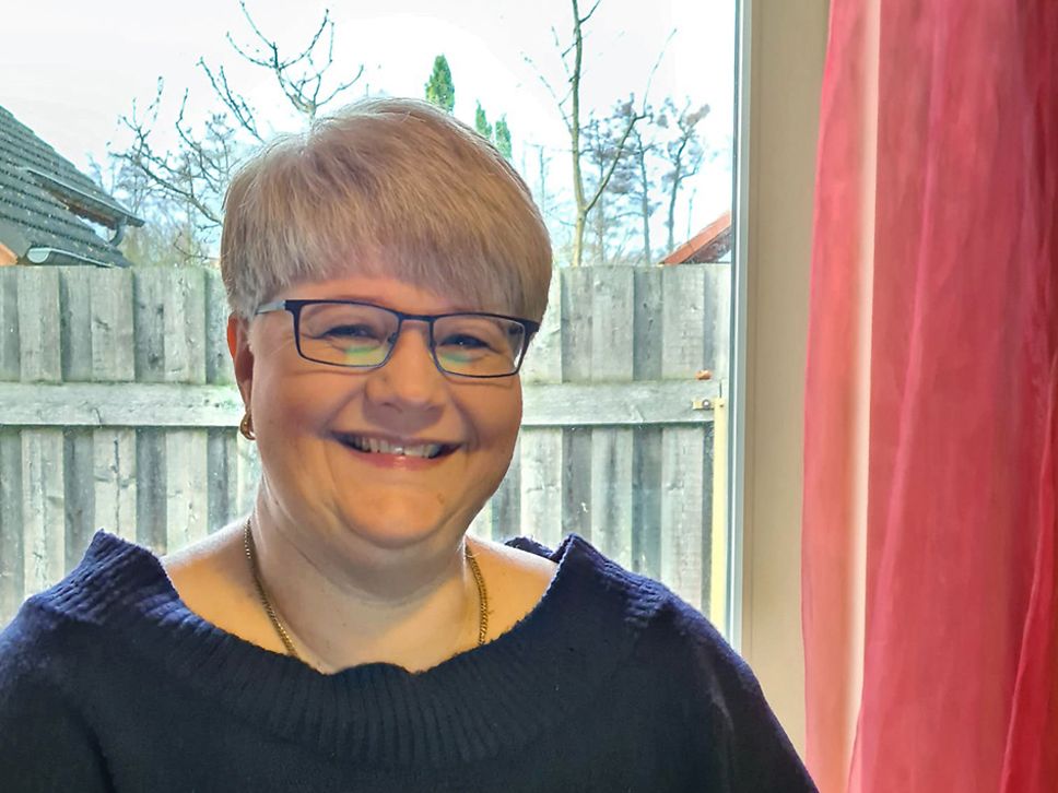 Suzanne Scherping sitzt an ihrem Arbeitsplatz im Homeoffice und lächelt in die Kamera.