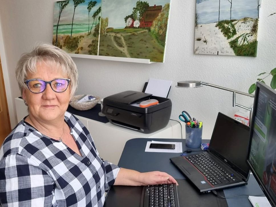 Annett Mueller sitzt an ihrem Arbeitsplatz im Homeoffice und schaut in die Kamera