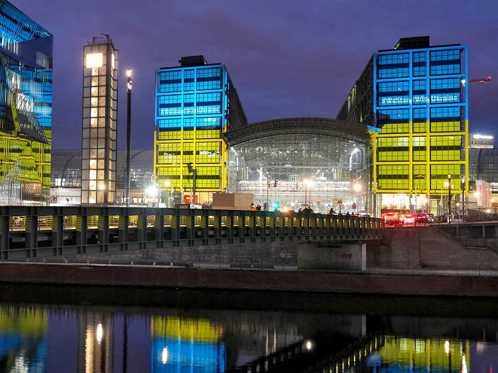 Frontansicht des Berliner Hauptbahnhofs. Er leuchtet in den Farben der ukrainischen Flagge - blau und gelb.