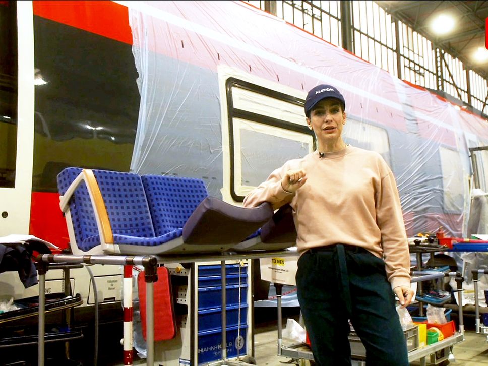 Moderatorin Nadine Heidenreich steht neben einem Zug und ausgebauten Sitzen.