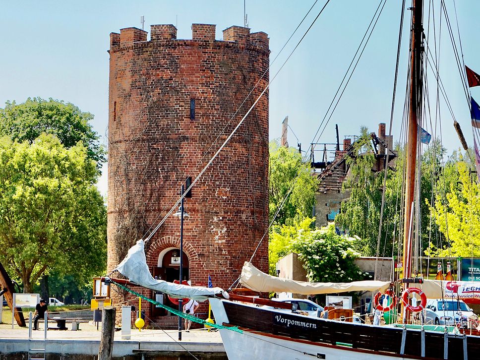 Ein alter Turm gemauert aus roten Steinen, davor ein Boot.