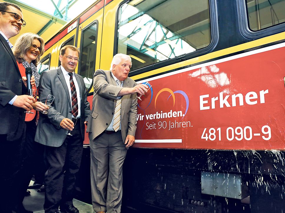Vier Personen stehen mit Sektgläsern vor einem mit dem Schriftzug "Erkner" beklebten S-Bahnzug