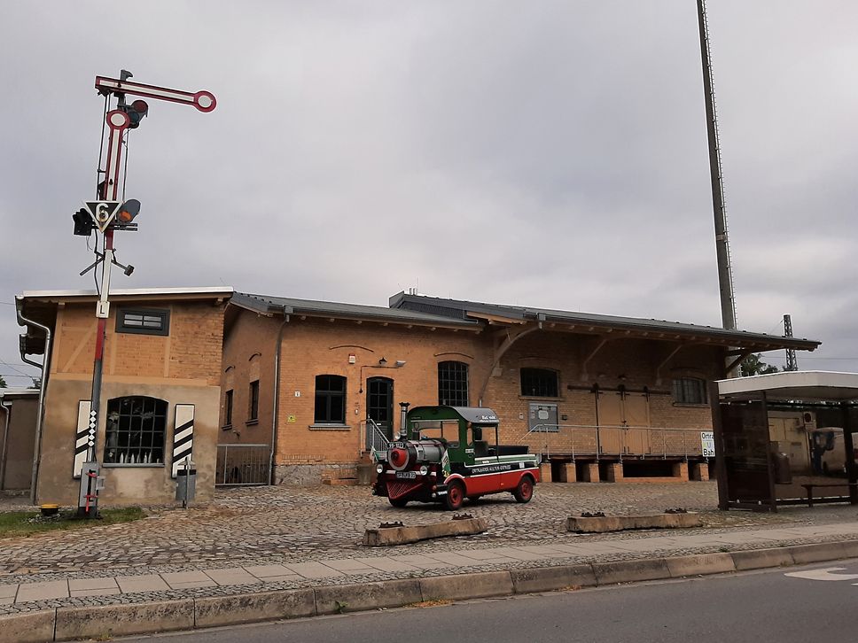 Ein historisches Gefährt steht vor einem Bahnhofsgebäude.