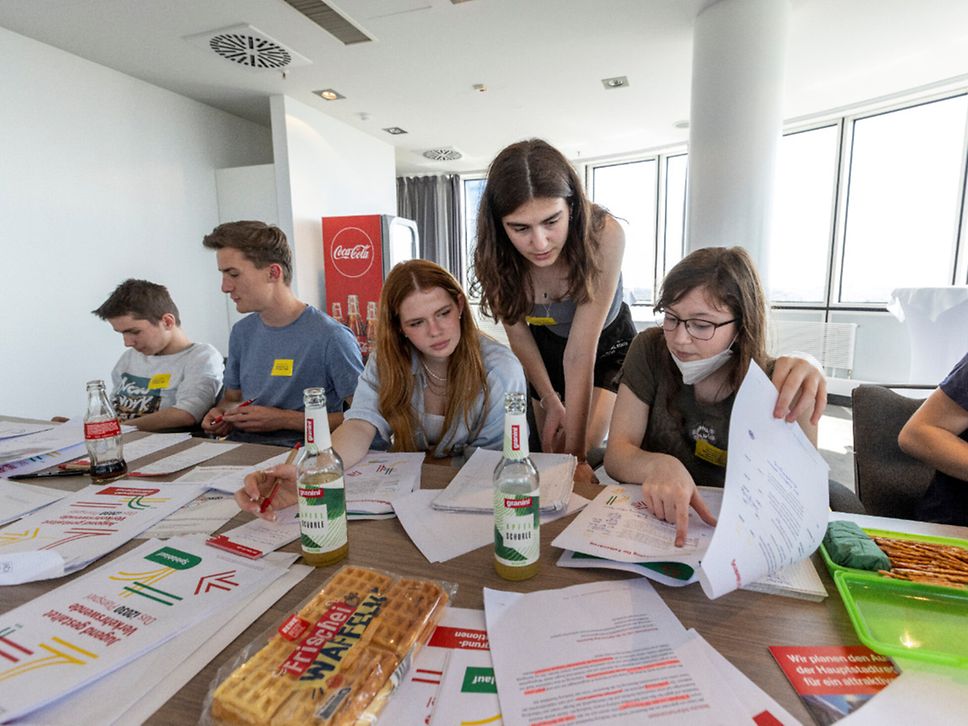 Eine Gruppe von Schüler:innen diskutiert über Unterlagen.