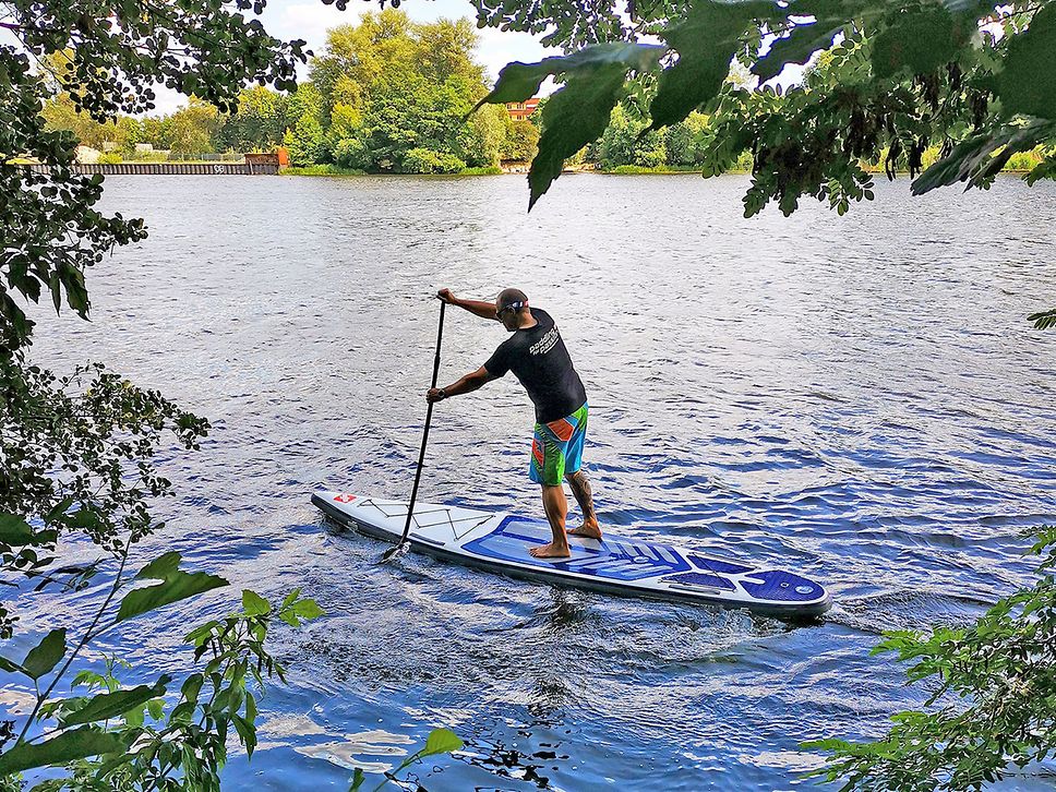 Mann fährt auf seinem SUP-Board auf dem Wasser.