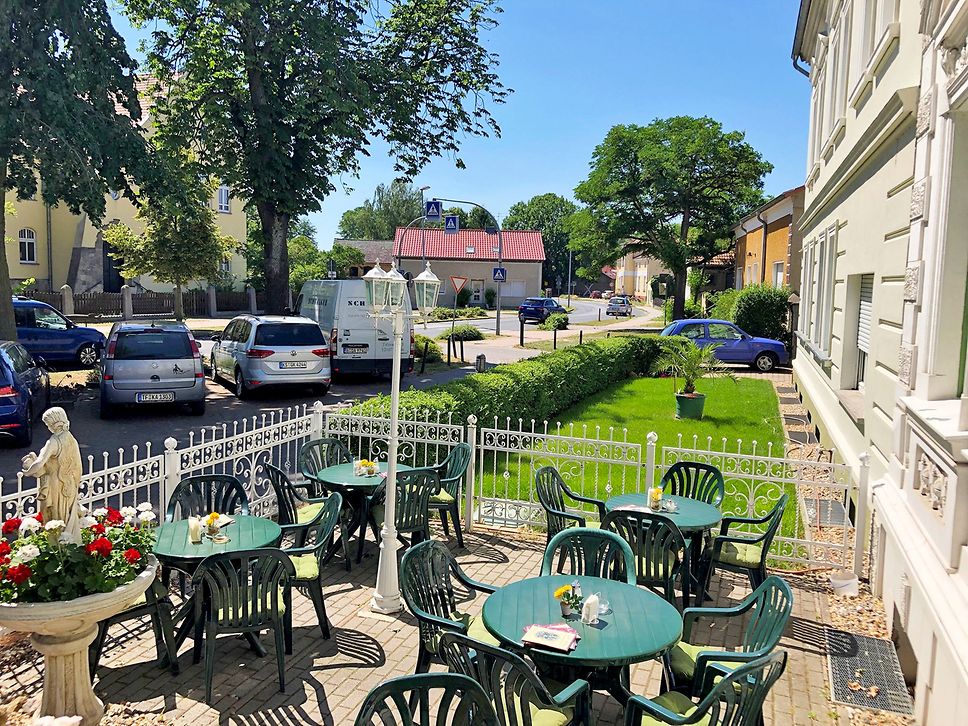 Terrasse eines Cafés mit grünen Sitzgruppen.