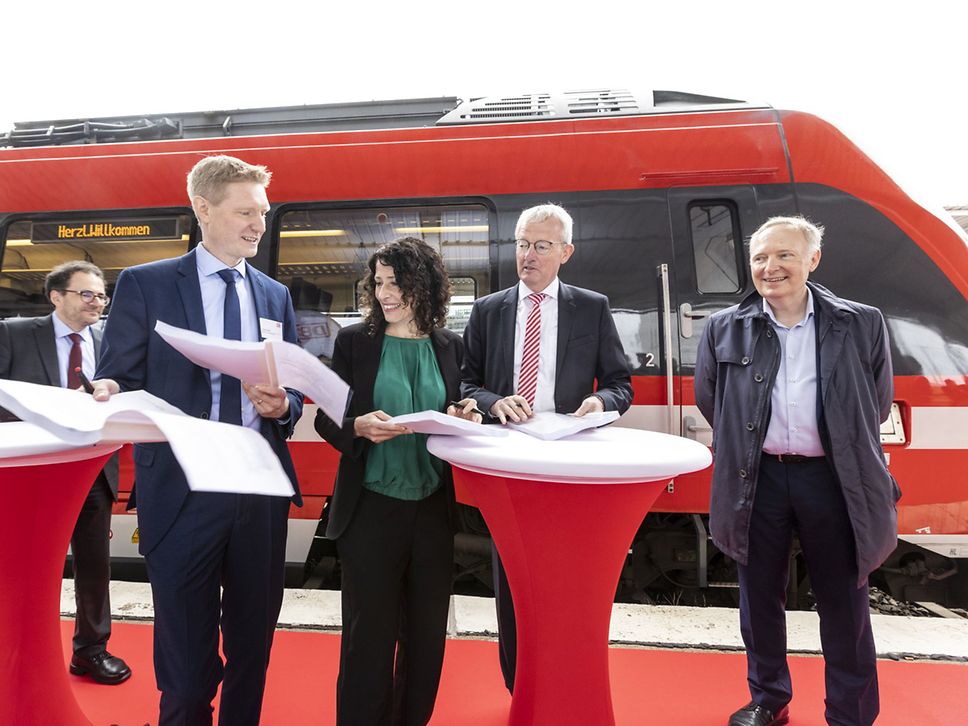 Vier Männer und eine Frau mit vielen Papieren in der Hand stehen vor einem roten Zug.