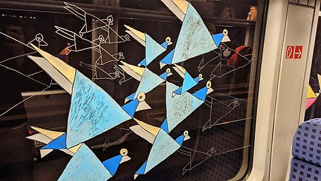 Fensterbild am Innenfenster eines Zuges, zu sehen sind blaue Vögel in abstrakter Form mit Körpern aus Dreiecken.