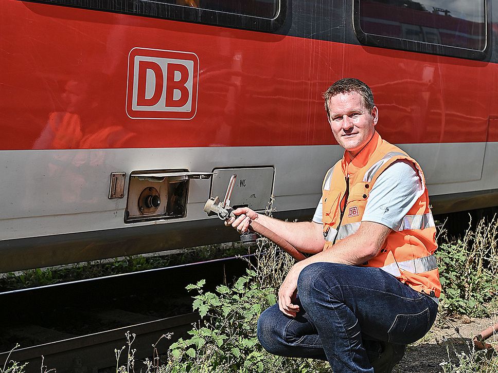 Ein Mann in orangefarbener Warnweste führt einen Schlauch zum Wasser-Füllstutzen am Zug.