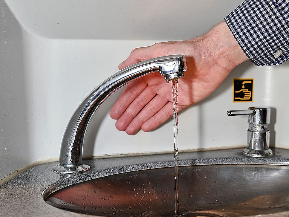 Eine Hand hinter einem Wasserhahn aus dem klares Wasser läuft.