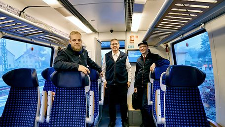 Drei Männer stehen in einem Fahrgastabteil eines Regionalzuges.
