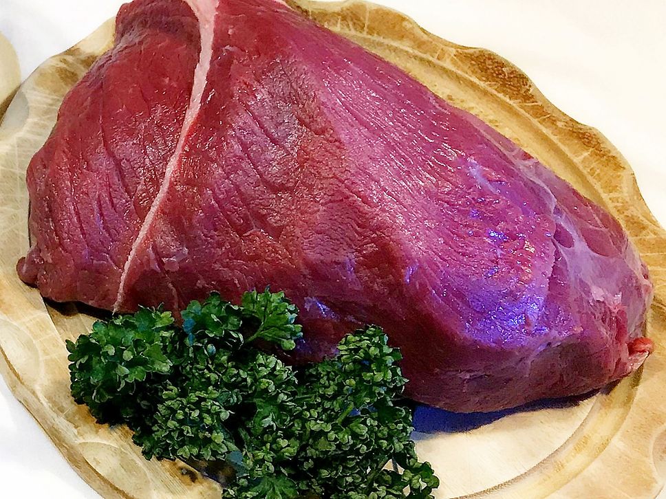 Ein Stück roher Büffelbraten liegt mit Petersilie angerichtet auf einem Holzbrett.