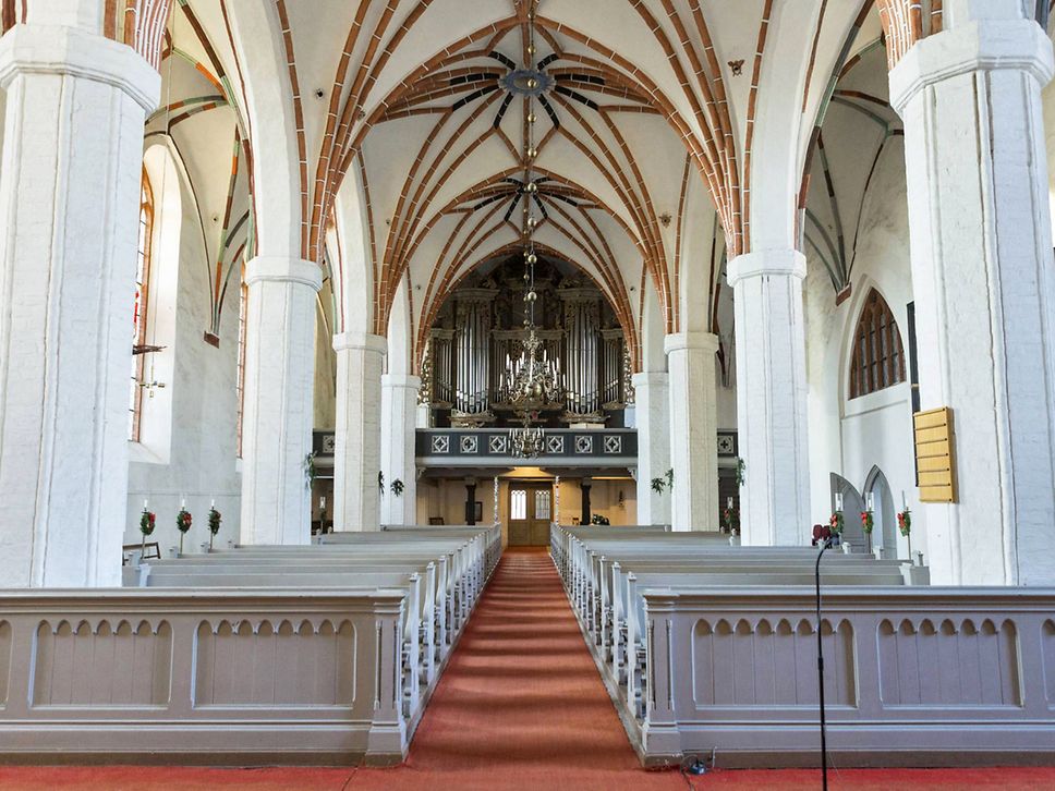 Blick in die Kirche St. Marien in Angermünde, links und rechts graue Kirchenbänke, im Hintergurnd eine Orgel.